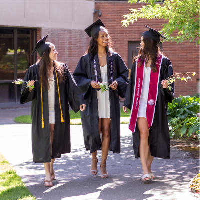 三位面带微笑的SPU女毕业生戴着帽子，穿着学士服，走在校园里